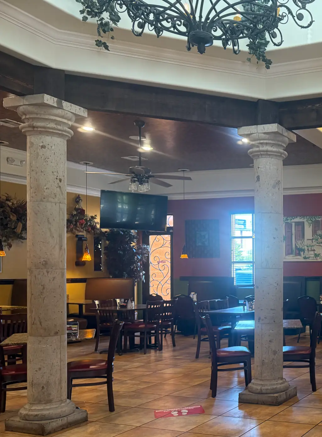 El comedor de Tink-A-Tako #12, 7507 Potranco Rd: un arco de columnas de cantera y vigas de madera oscura, con las mesas puestas al fondo