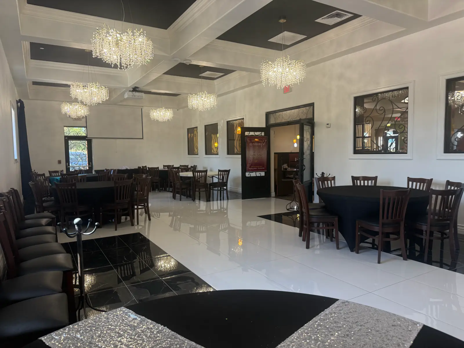 El salón de eventos de Sandra's Cuisine: candiles de cristal bajo un techo artesonado, piso de mármol blanco y negro y mesas redondas listas para la fiesta