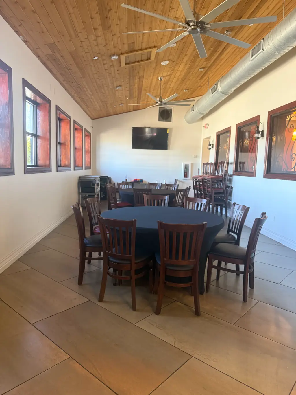 El segundo salón de Sandra's Cuisine: techo de duela de madera con ventiladores, ventanas con marco rojo y una mesa redonda con sillas de madera oscura